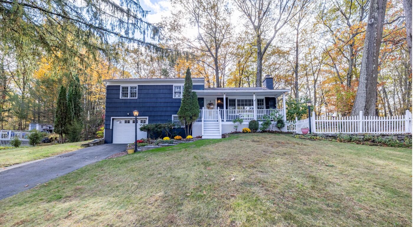 The Well's Danbury house: a navy two-level home with a front porch and white fence, set in the woods.