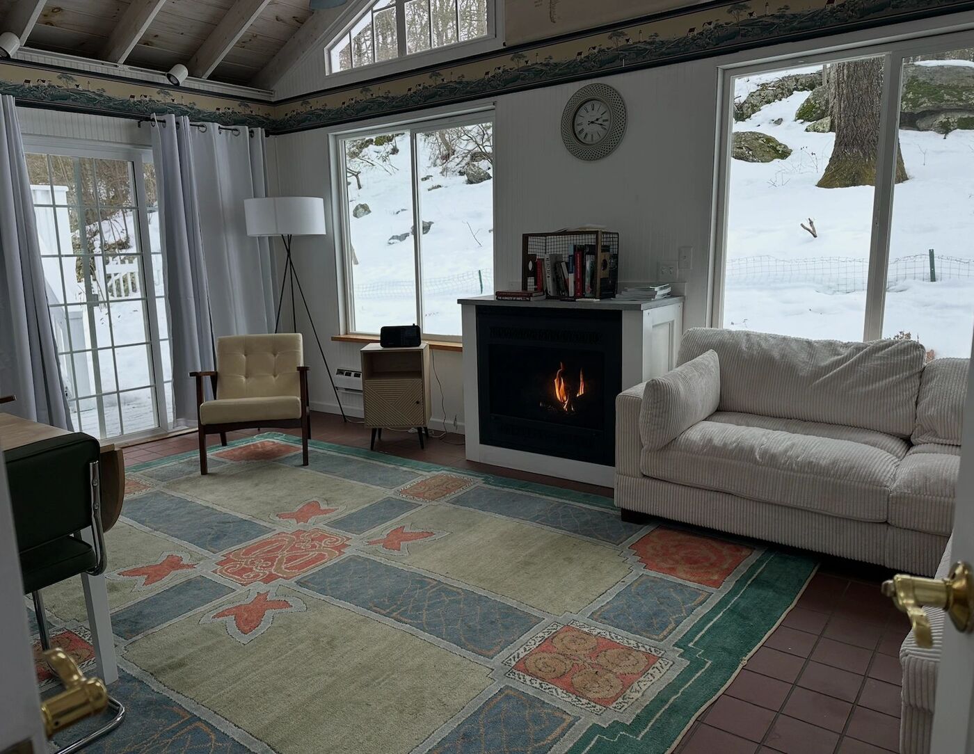 The common room, with a fireplace and a sofa, looking out to snowy woods.